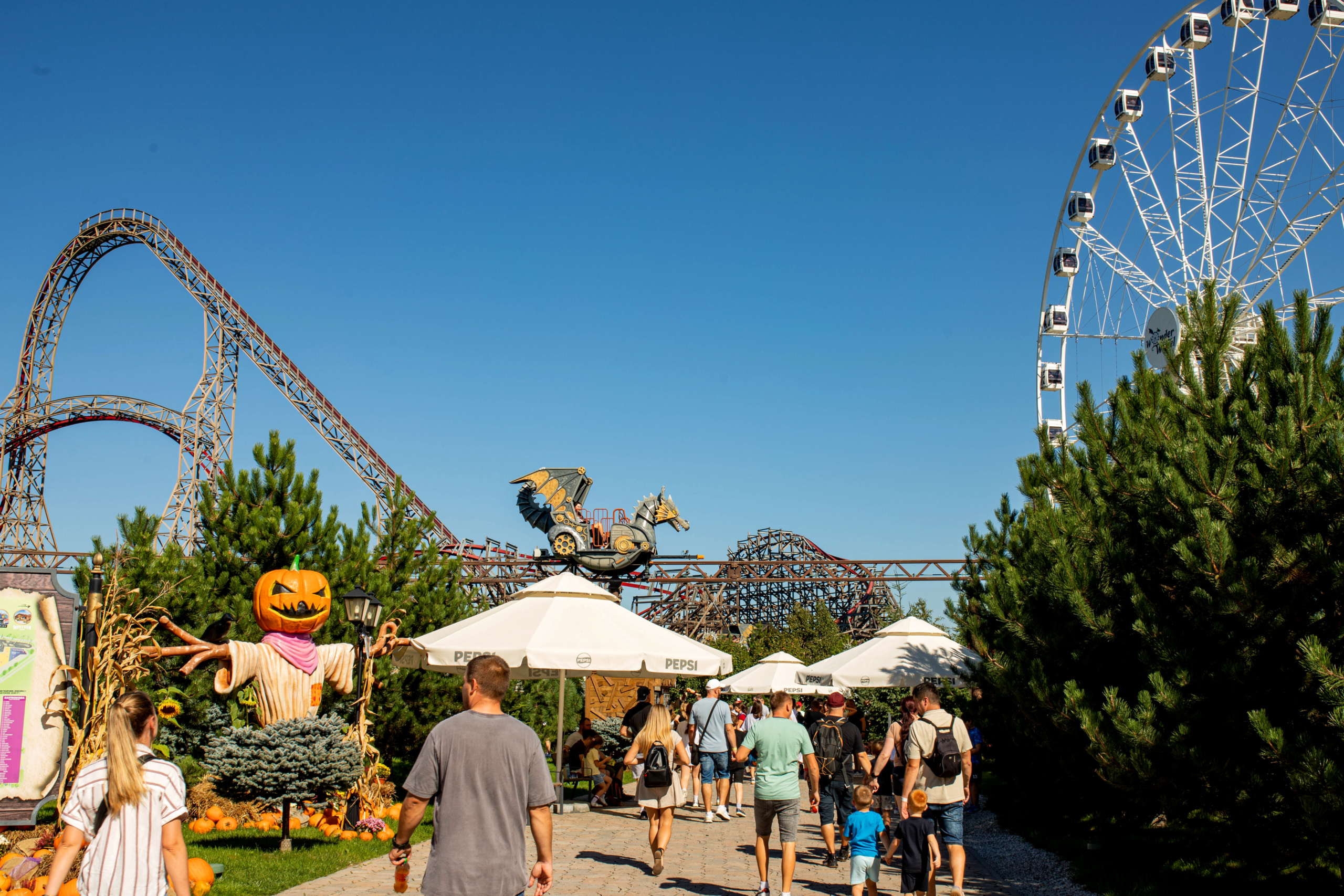 Amusement park skyline coaster + Ferris wheel Energylandia main avenue with seasonal pumpkin decorations, roller coaster skyline and Ferris wheel in the background.